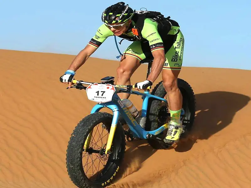 Mountain biker riding through the High Atlas Mountains towards the Moroccan desert, passing Berber villages and dramatic red-rock landscapes.