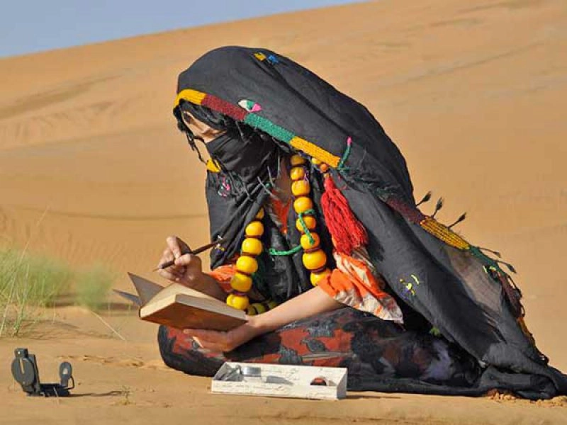 A woman standing in the vast Sahara Desert, surrounded by golden dunes under a clear Moroccan sky, capturing the serenity and beauty of the desert landscape.